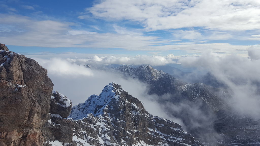 Blick vom Zugspitzgipfel auf verschneite Berggipfel über den Wolken