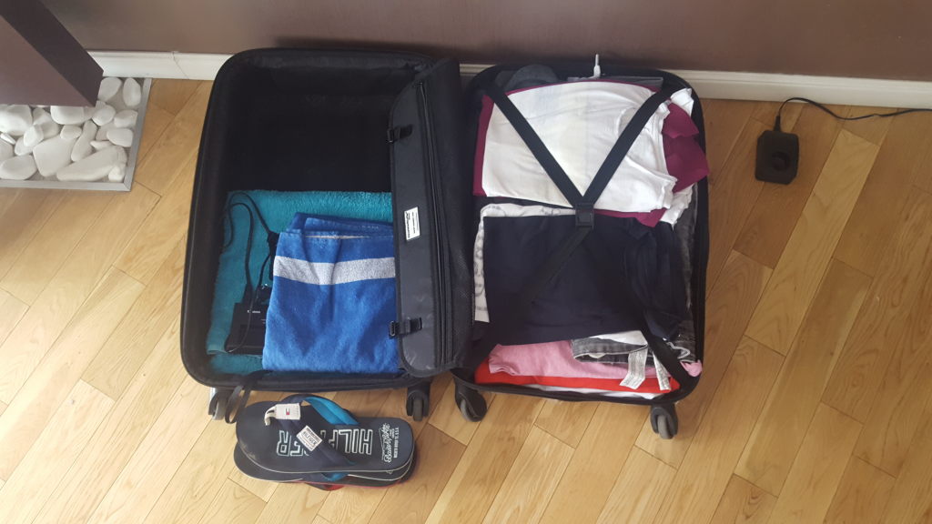 Geöffneter Koffer mit Kleidung und Strandtüchern auf Holzboden