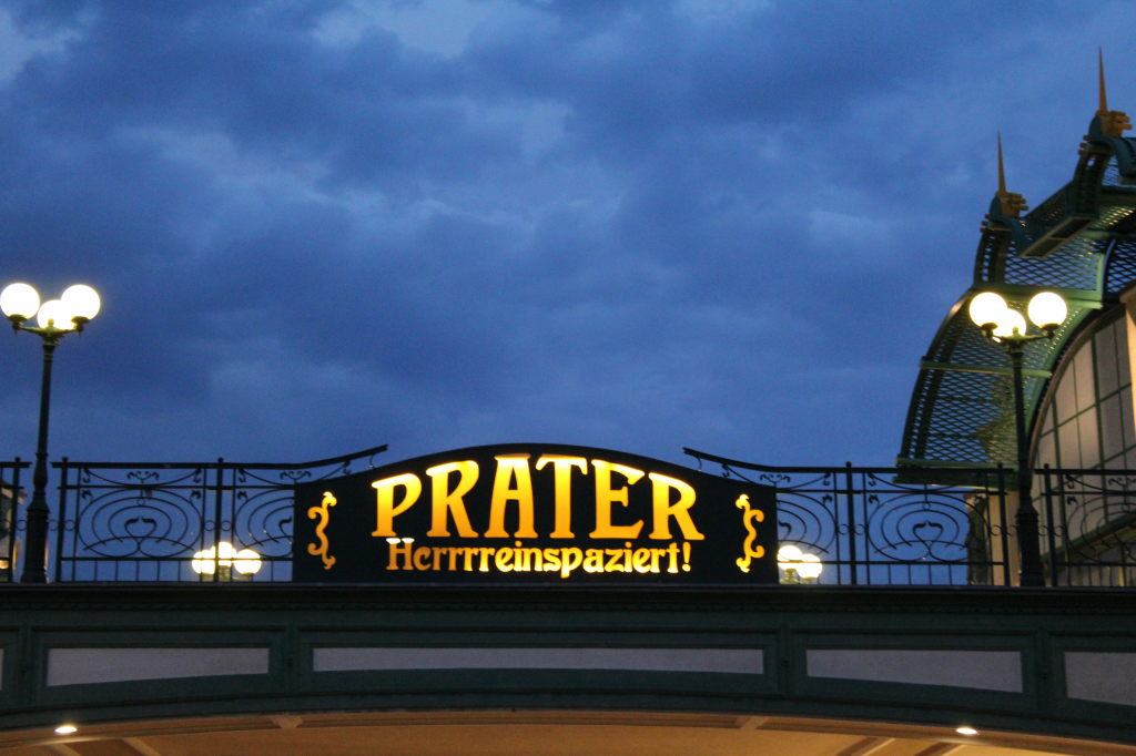 Beleuchtetes Prater-Eingangsschild mit Schriftzug "Herrrreinspaziert!" in Wien bei Nacht