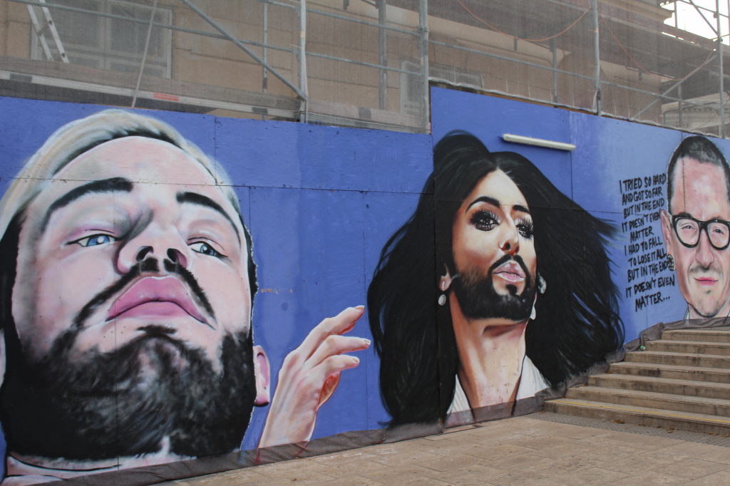 Großes Street-Art-Mural mit drei Porträts auf blauer Wand in Wien