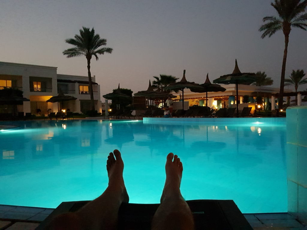 Beleuchteter Hotelpool in Scharm El-Scheich am Abend mit Palmen und Strohdach-Sonnenschirmen
