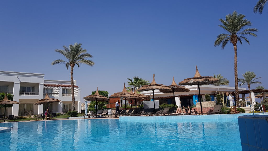 Hotelpool in Scharm El-Scheich mit Palmen, Strohdach-Sonnenschirmen und weißen Hotelgebäuden