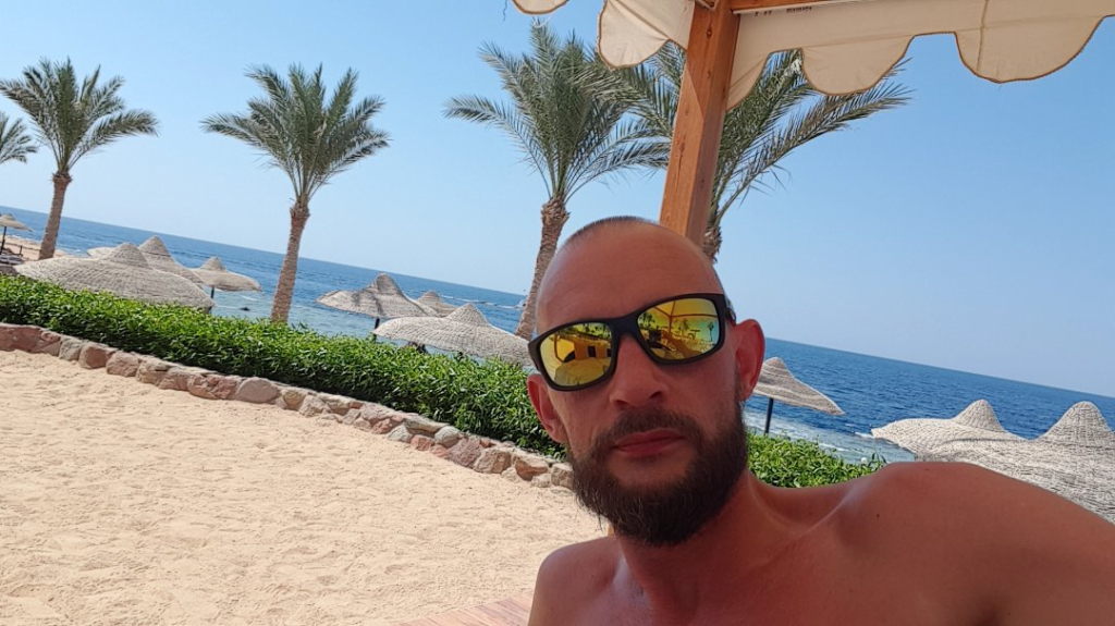 Mann mit Sonnenbrille am Strand von Scharm El-Scheich mit Palmen und Roten Meer