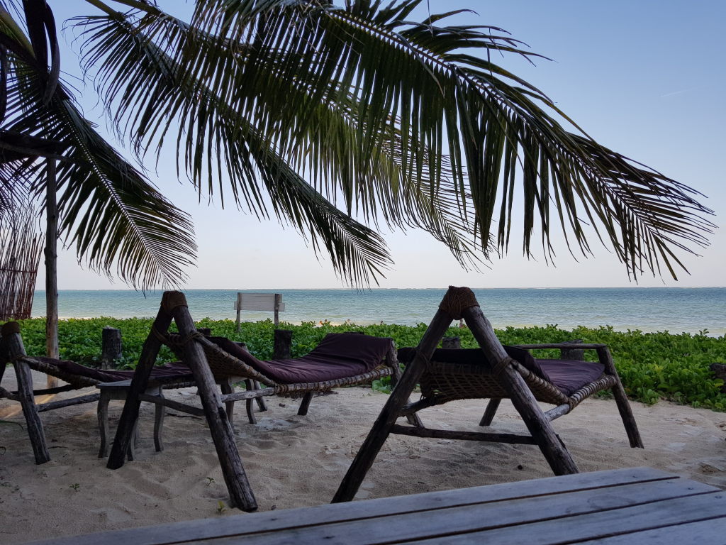 Rustikale Holzliegestühle unter Palmen am Sandstrand von Sansibar mit Meerblick