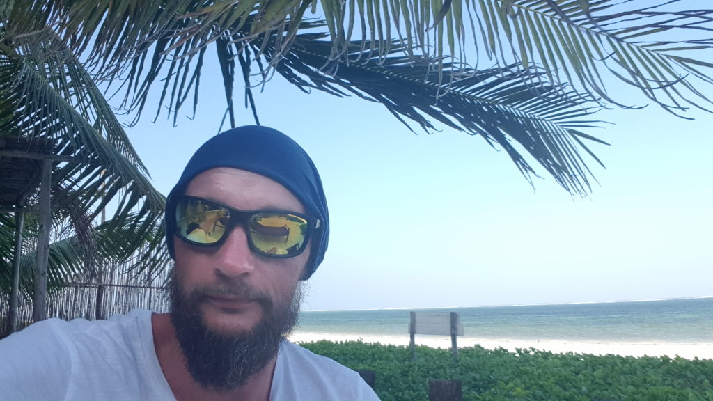 Mann mit Sonnenbrille und Beanie am Strand von Sansibar unter Palmen