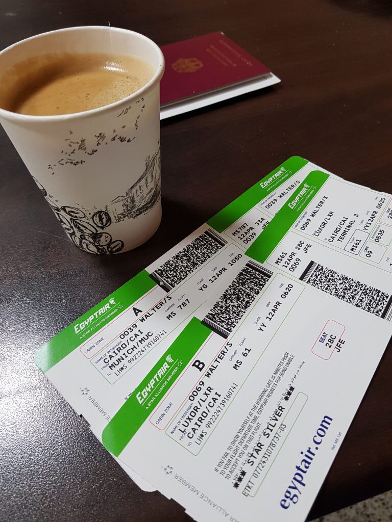 Zwei EgyptAir Boardingpässe für Luxor–Kairo–München neben einem Kaffeebecher und Reisepass