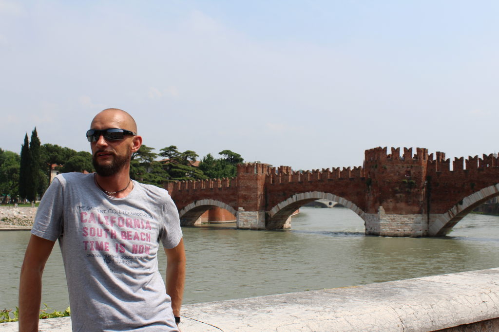 Mann mit Sonnenbrille vor der Castelvecchio Brücke in Verona über die Etsch