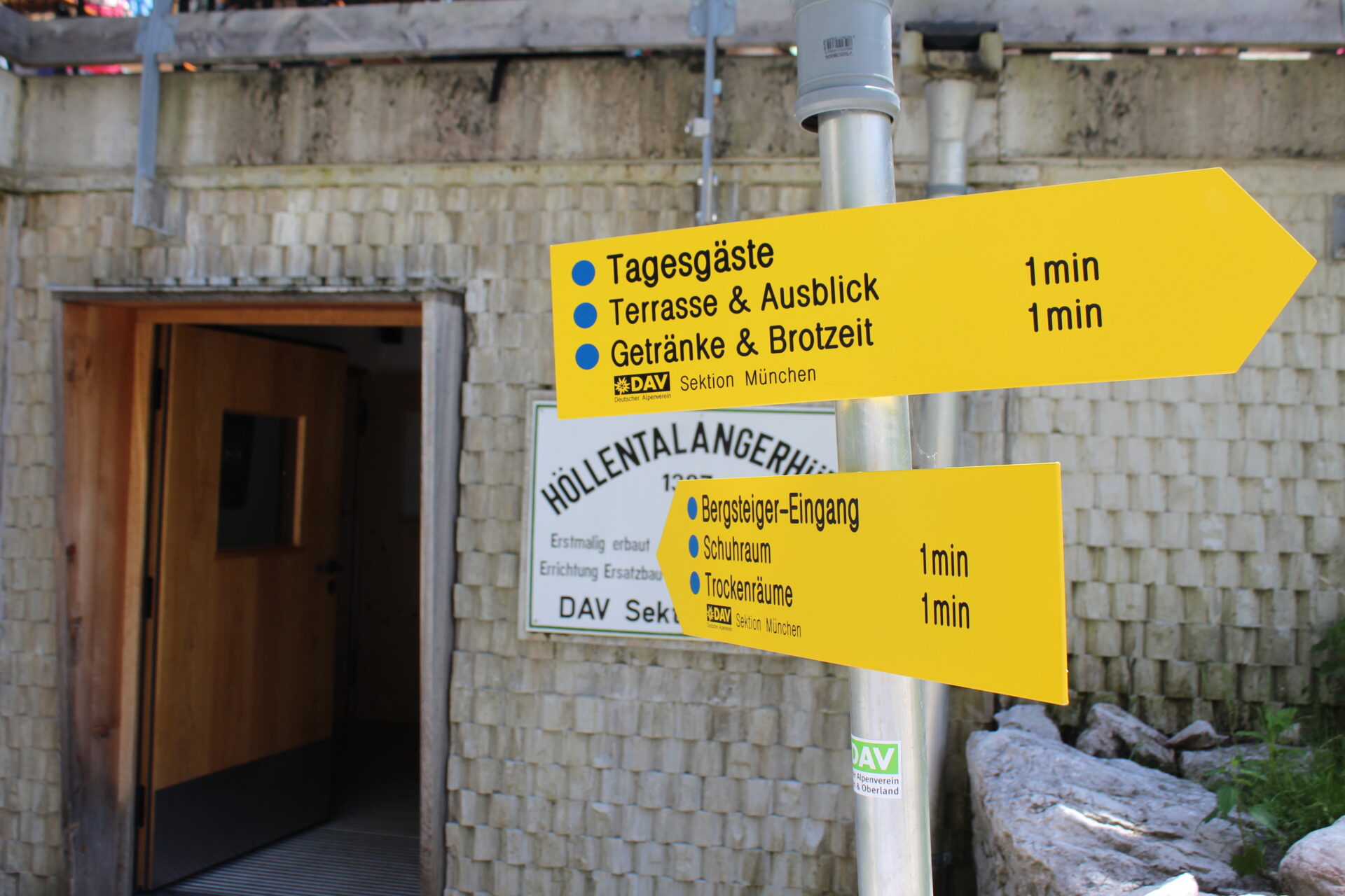 Gelber Wegweiser an der Höllentalangerhütte mit Hinweisen für Tagesgäste