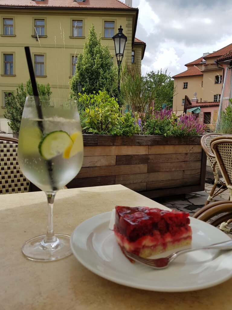 Erdbeer-Kuchen und Gurken-Drink auf Café-Terrasse in Prag mit historischen Häusern
