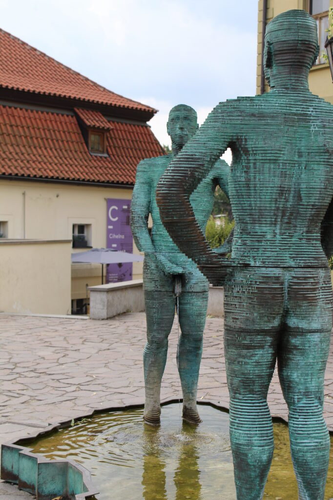 Zwei grüne Bronzeskulpturen 'Čůrající postavy' an einem Brunnen in Prag