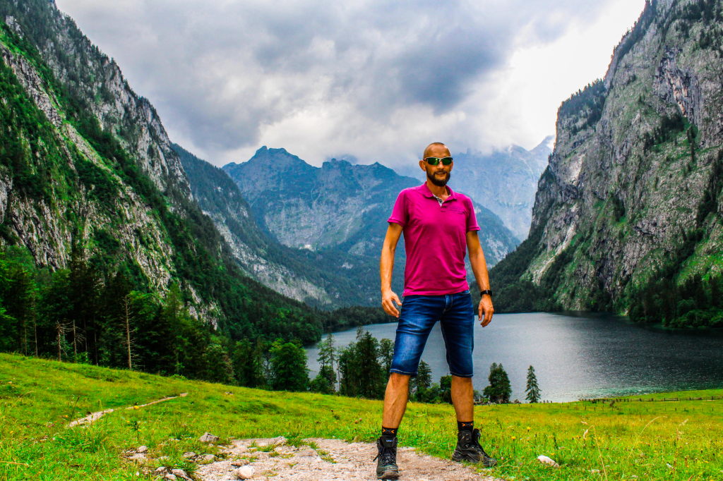 Mann in pinkem Poloshirt vor dem Obersee am Königssee mit Bergpanorama