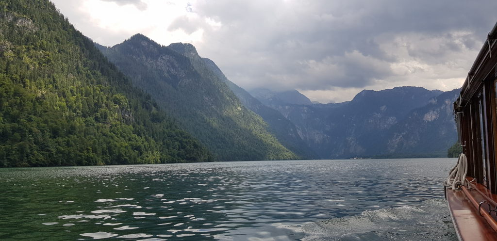 Blick vom Ausflugsboot auf den Königssee mit bewaldeten Bergen und bewölktem Himmel