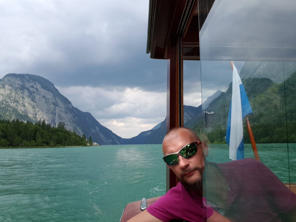 Mann mit Sonnenbrille auf dem Elektroboot der Schifffahrt Königssee mit türkisem See und Bergpanorama