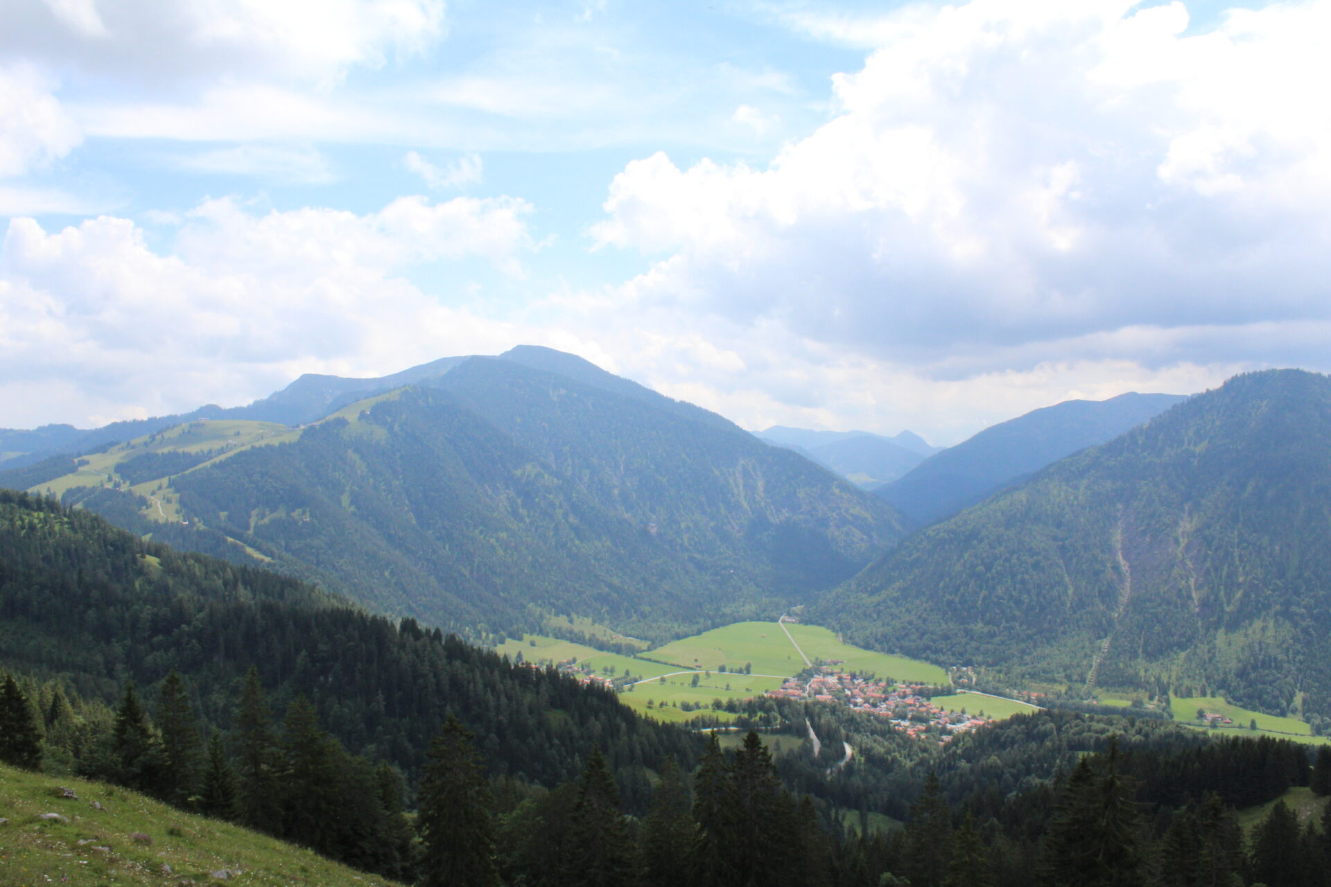 Panoramablick vom Wendelstein ins Tal mit kleinem Bergdorf und bewaldeten Berghängen