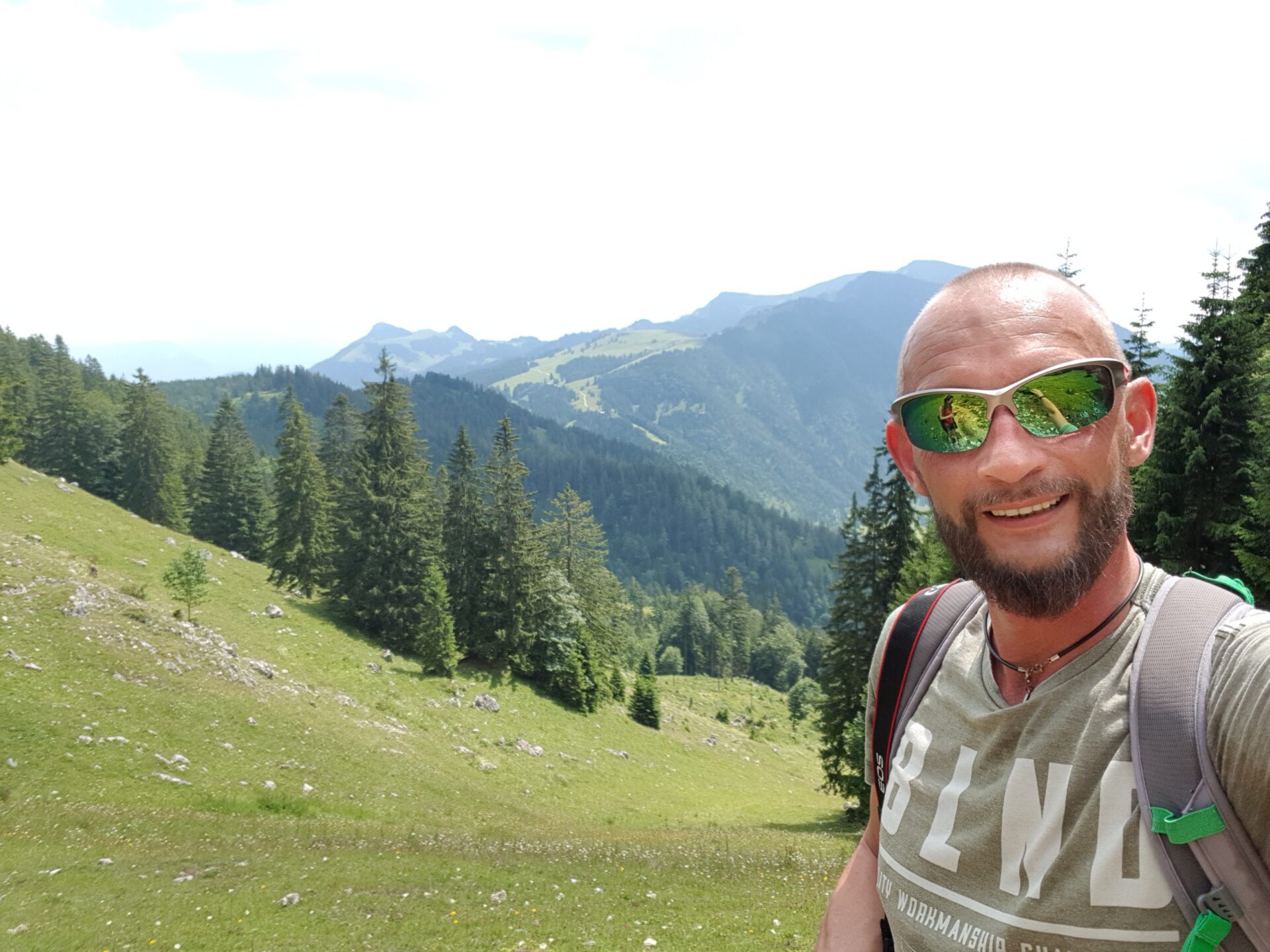 Wanderer mit Sonnenbrille und Rucksack beim Selfie am Wendelstein mit Alpenpanorama