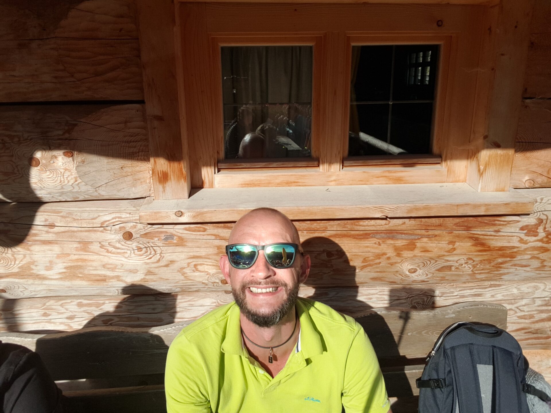 Mann mit Sonnenbrille sitzt lachend vor Holzfassade der Kolbensattelhütte