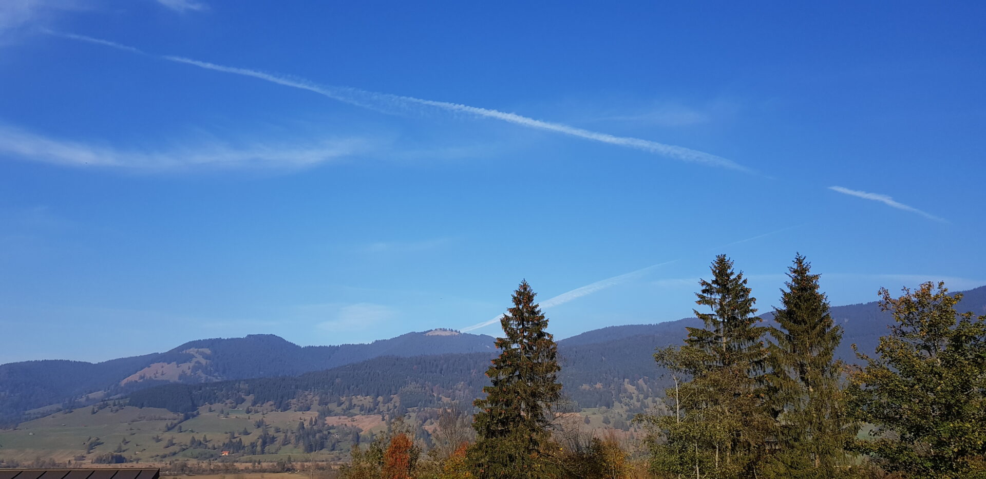 Weitblick auf bewaldete Berge bei Oberammergau im Herbst mit blauem Himmel