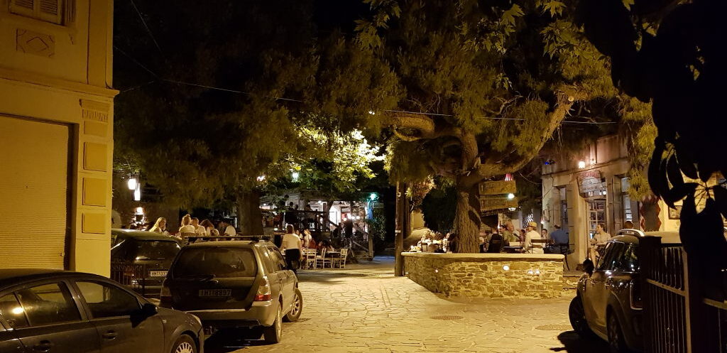 Belebter Dorfplatz in Nikiti bei Nacht mit Restaurants und alten Bäumen