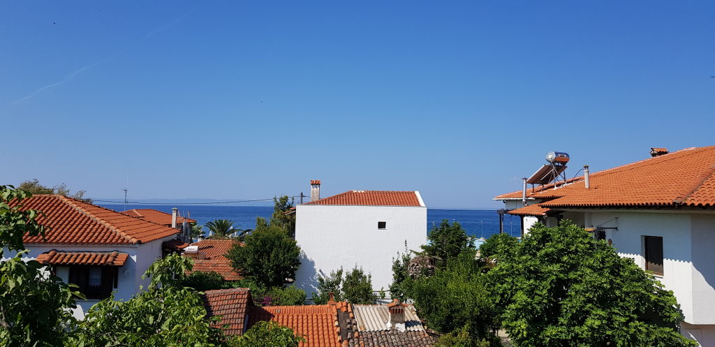 Blick über weiße Häuser mit roten Ziegeldächern auf das blaue Meer in Nikiti, Griechenland