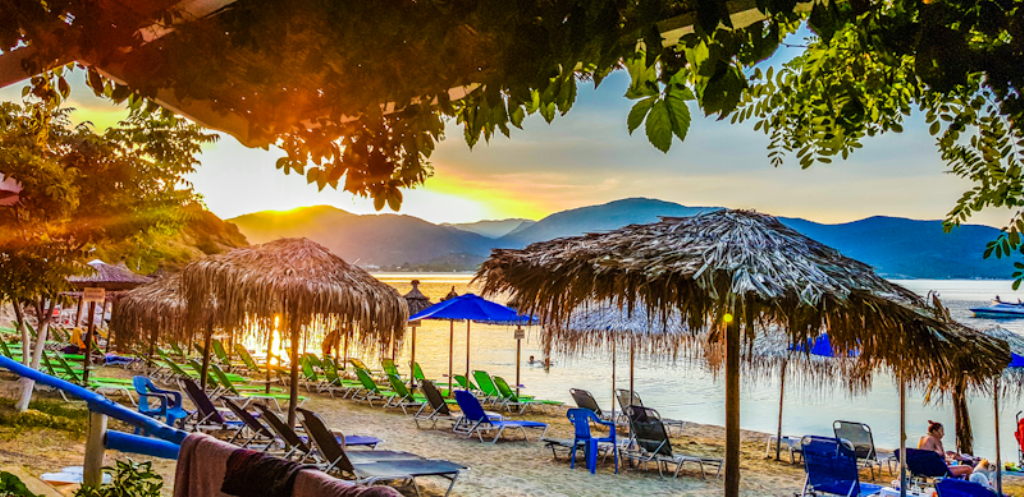 Sandstrand Tourkolimnionas Nikiti mit Strohdach-Sonnenschirmen und Sonnenuntergang über Bergen