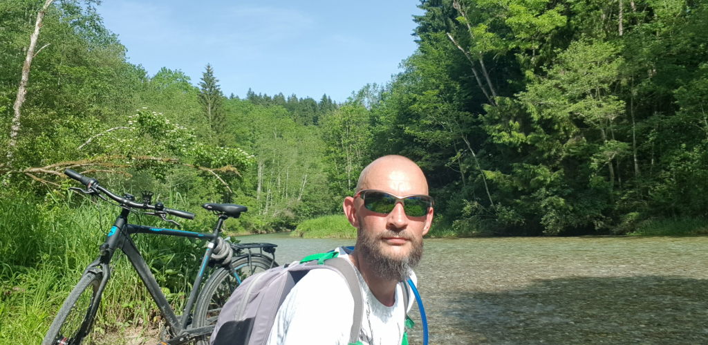 Mann mit Fahrrad und Rucksack am Fluss beim Spiralschacht Thalham