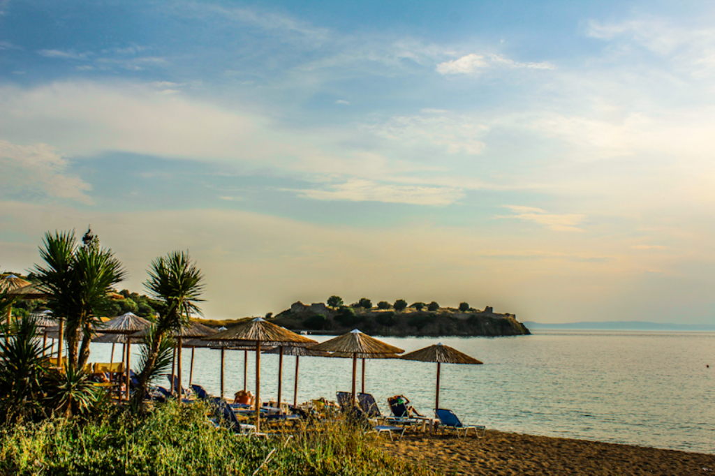 Toroni Beach Sithonia mit Strohhut-Sonnenschirmen, Liegestühlen und Ruine im Hintergrund