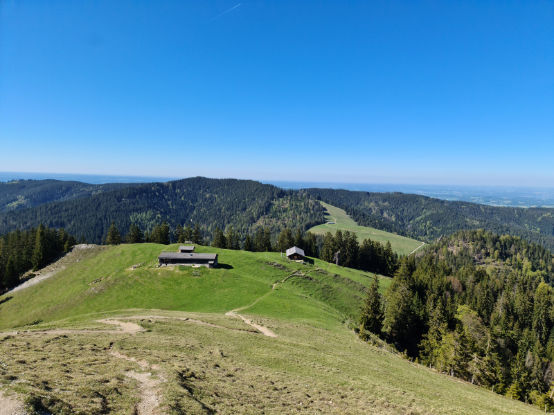 Blick vom Baumgartenschneid auf eine Almhütte im Vordergrund und die Voralpenlandschaft dahinter