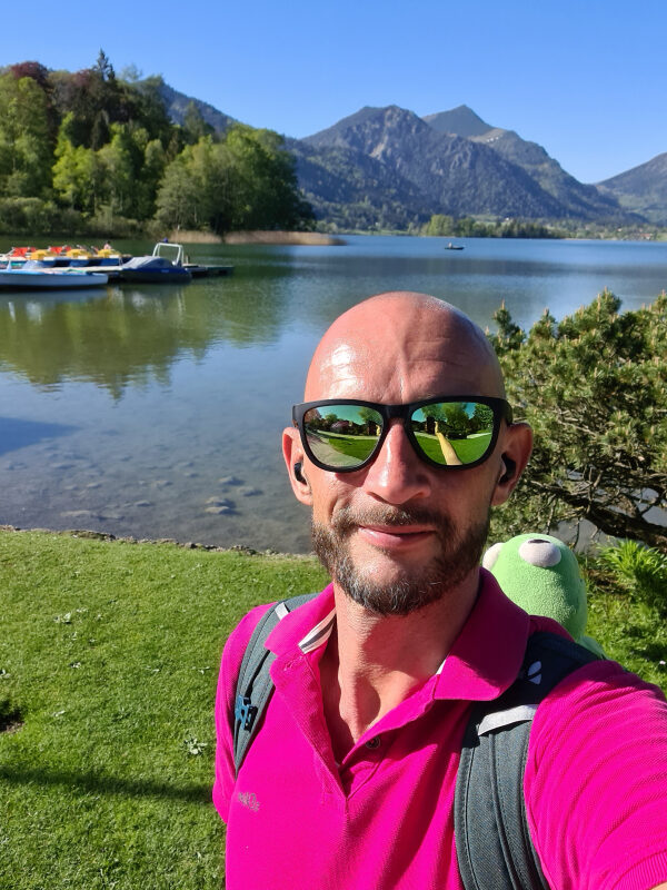 Sebastian mit Kermit am Schliersee-Ufer, dahinter Tretboote und die Berge