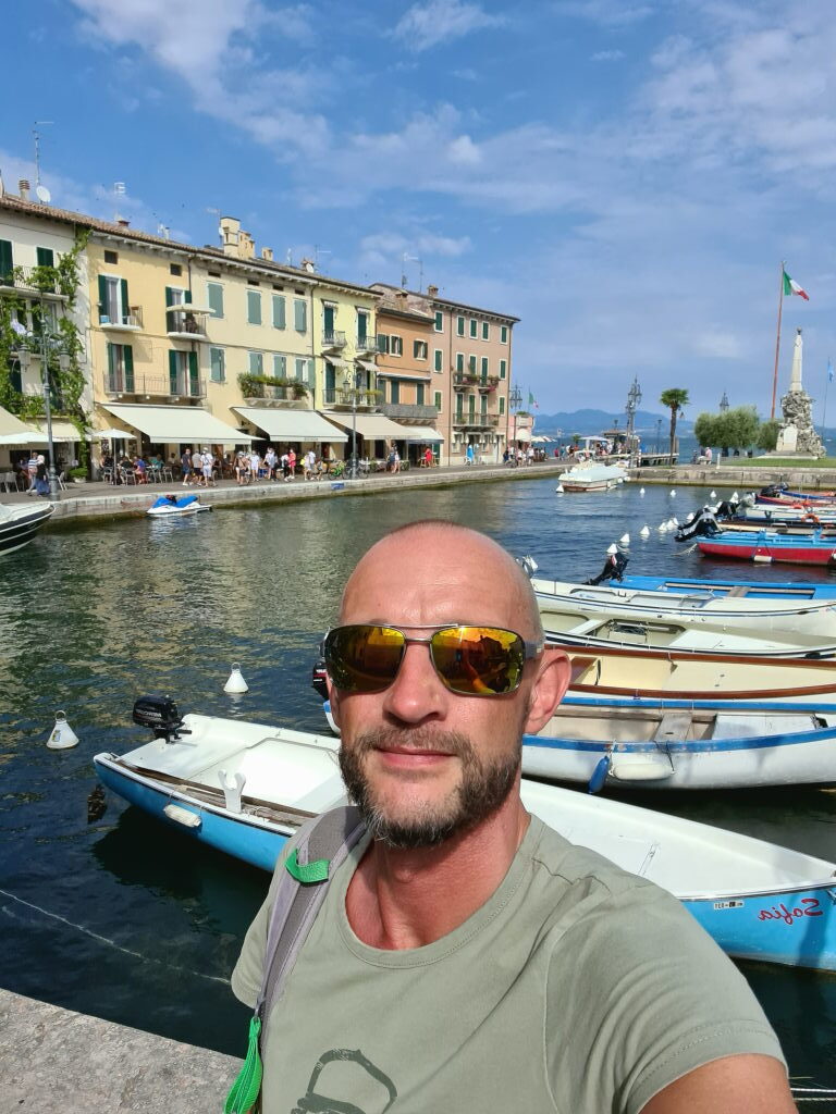 Selfie im Hafen von Lazise am Gardasee mit bunten Häuserfassaden und Booten im Hintergrund