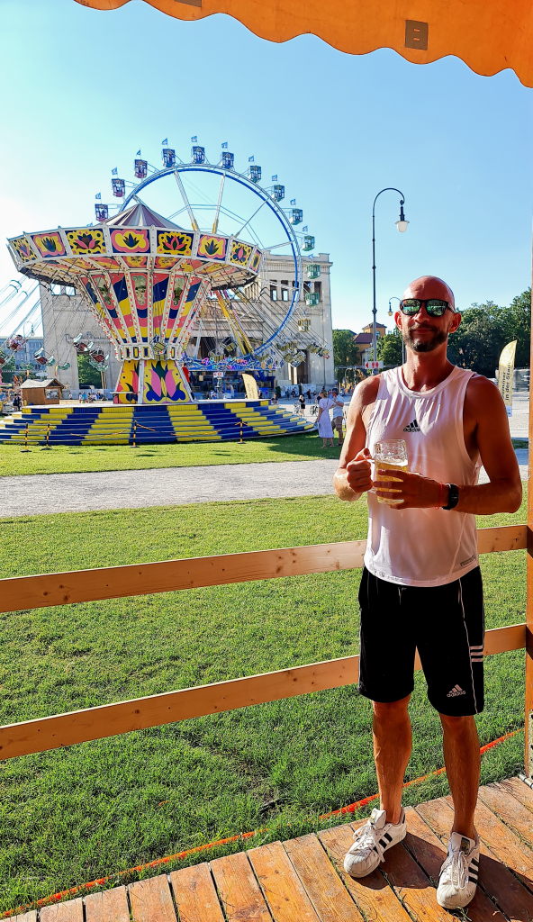 Sebastian mit Masskrug Bier vor Kettenkarussell am Königsplatz München, Sommer August 2020