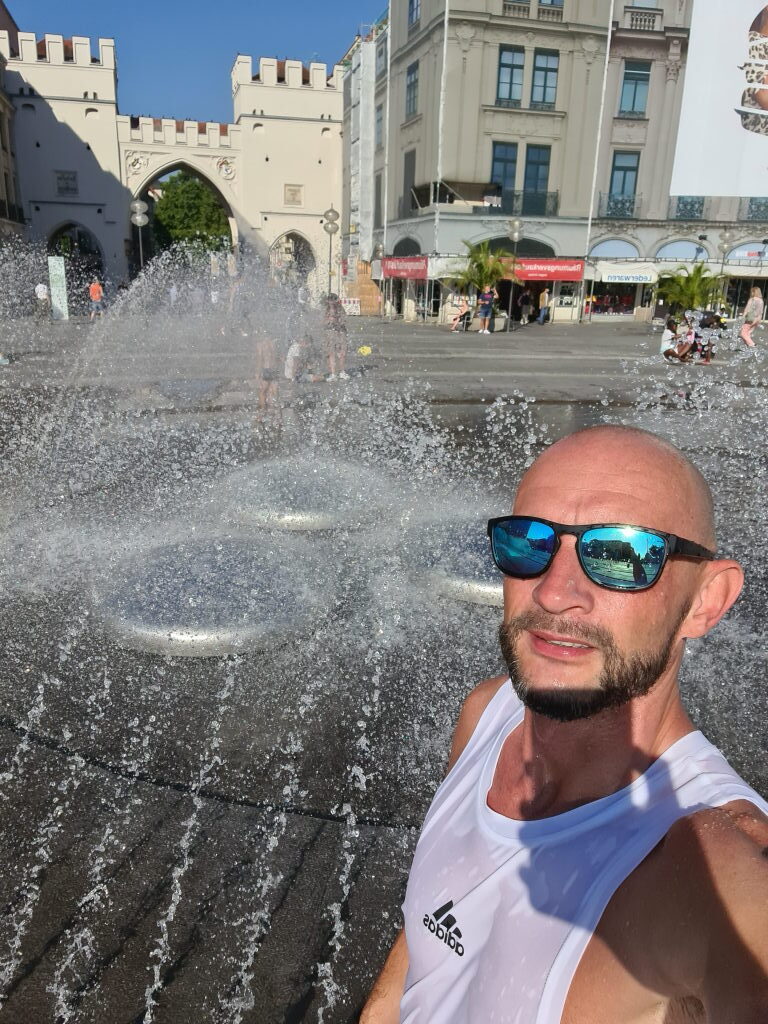 Sebastian Selfie im Stachus Brunnen München mit Wasserfontänen und Karlstor im Hintergrund, August 2020