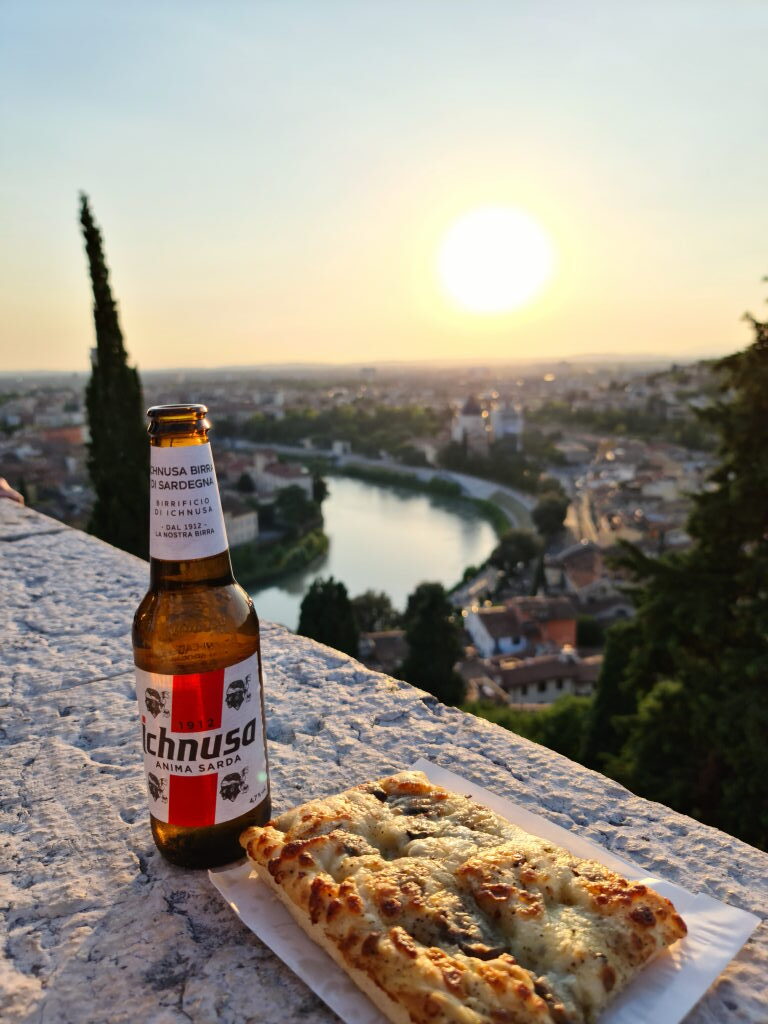 Ichnusa Bier und Pizza auf der Brüstungsmauer am Castel San Pietro mit Verona-Panorama und untergehender Sonne im Hintergrund