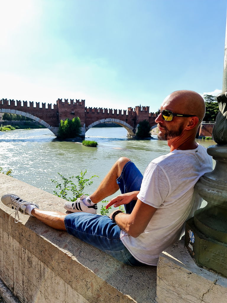 Sebastian sitzt entspannt an der Etsch-Brüstung mit Blick auf den Ponte Scaligero in Verona