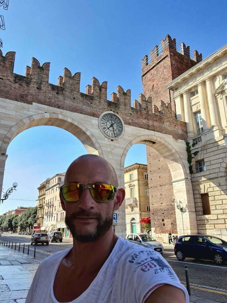 Selfie vor den Portoni della Brà in Verona mit Zinnenturm und Uhr im Hintergrund