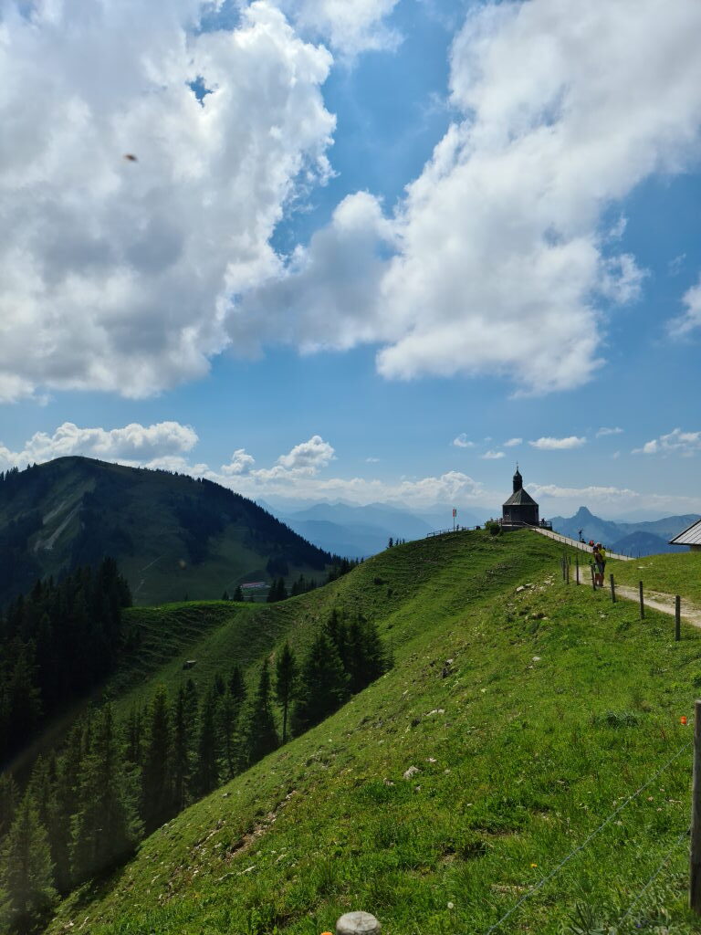 Kapelle Heilig Kreuz auf dem Wallberg-Kamm mit Bergpanorama und bewölktem Himmel