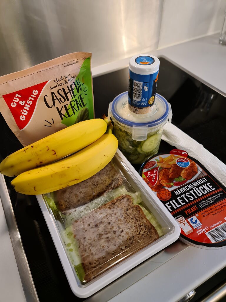 Wanderverpflegung: Vollkornbrote, Gurkensalat, Hähnchen-Filetstücke, Bananen und Cashewkerne