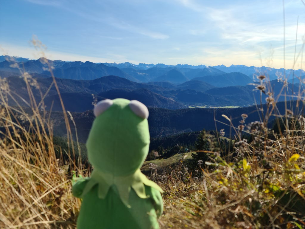 Kermit der Frosch blickt auf das Panorama der Bayerischen Alpen vom Brauneck-Gipfel im Oktober 2020