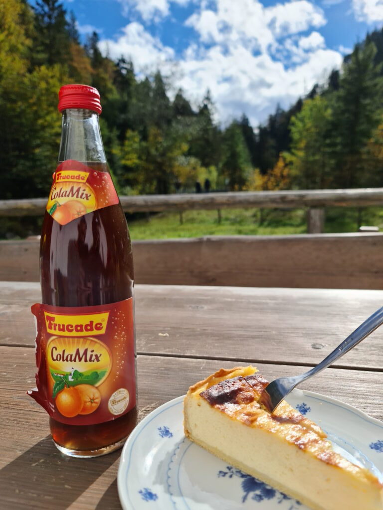 Käsekuchen und Trucade ColaMix Flasche auf Holztisch der Lainlalm mit Herbstblick Oktober 2020