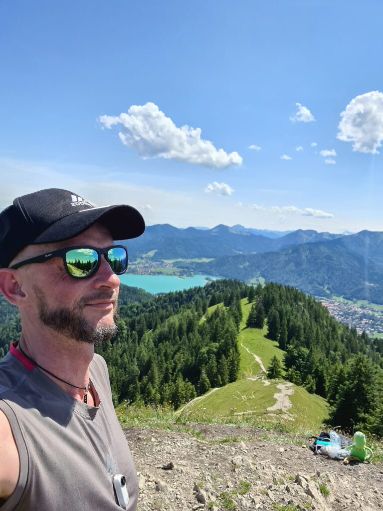 Sebastian am Gipfel des Baumgartenschneid mit türkisem Tegernsee und Bergpanorama im Hintergrund