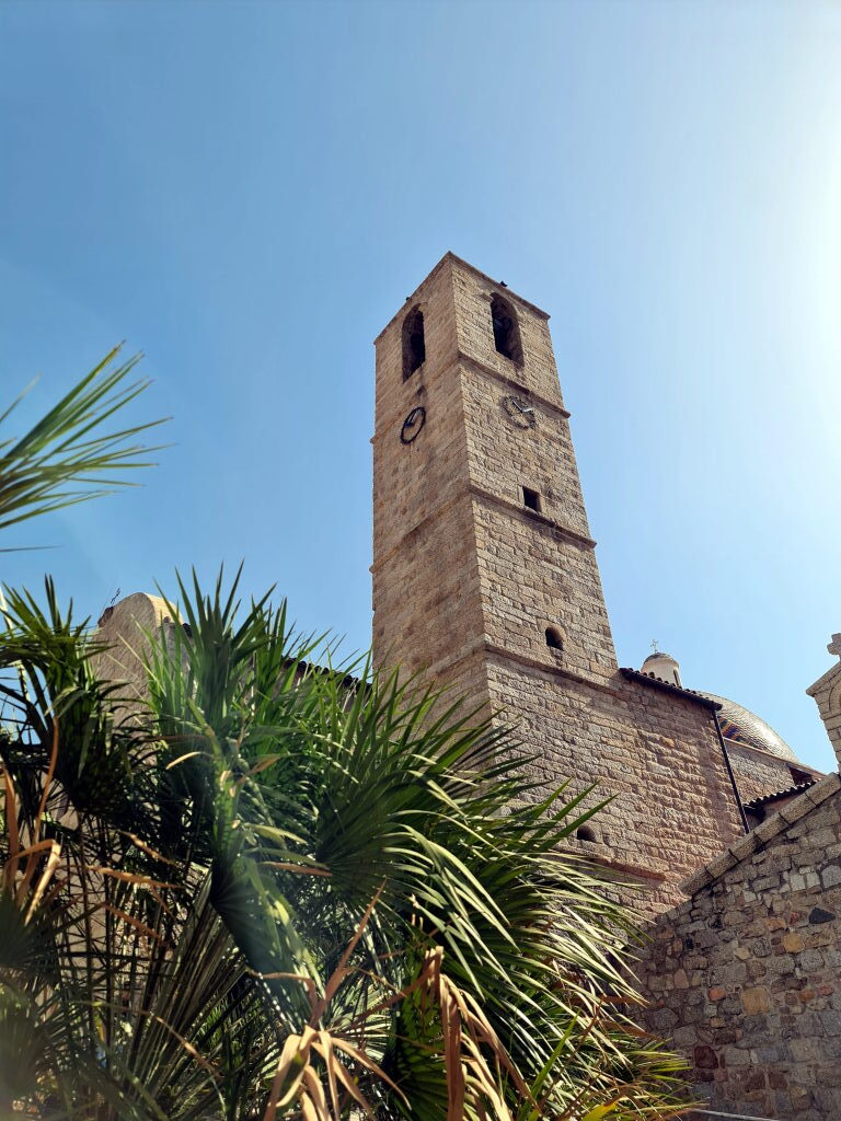 Glockenturm der Kathedrale San Simplicio in Olbia aus Granit, mit Palmen im Vordergrund
