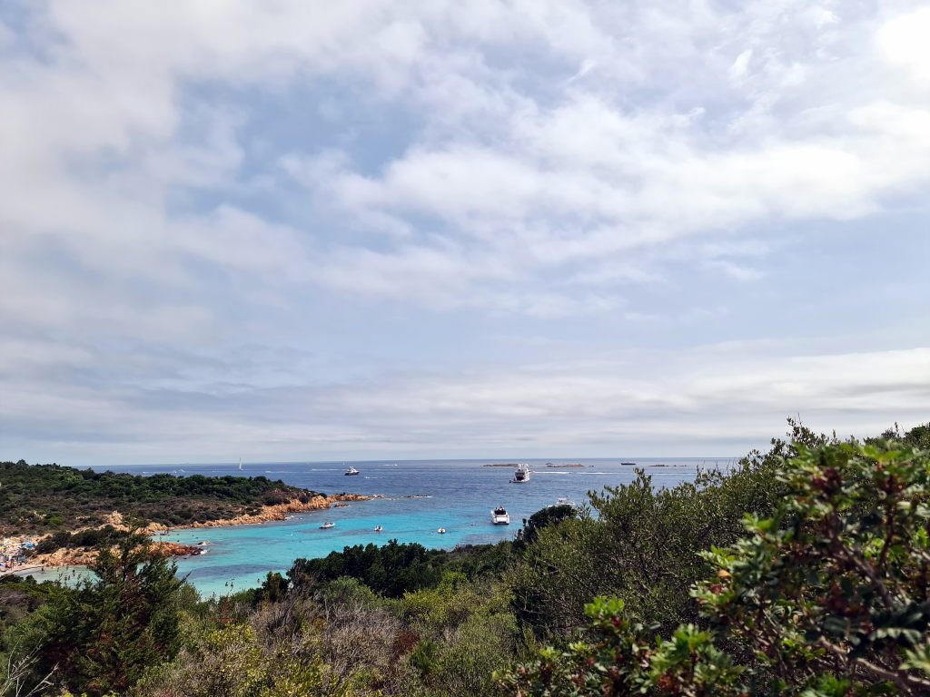 Blick vom Aussichtspunkt Costa Smeralda auf eine türkisblaue Bucht mit Booten und Macchia-Vegetation im Vordergrund