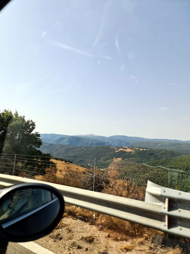 Bergpanorama der Costa Smeralda in Sardinien mit grünen Hügeln und trockenem Gras, durch das Autofenster fotografiert