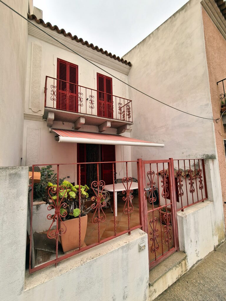 Sardisches Haus in Santa Teresa Gallura mit rotem Schmiedeeisen-Balkon, roter Markise und Sukkulenten im Vordergrund
