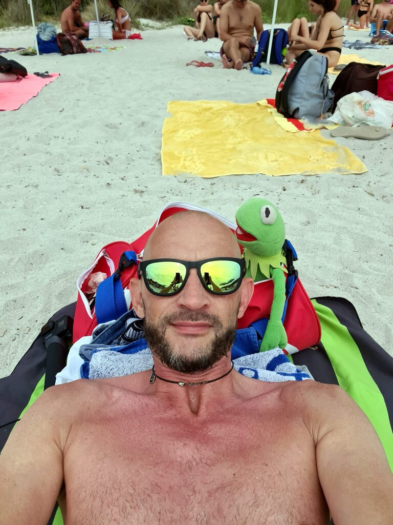 Selfie von Sebastian mit Sonnenbrille am Strand Spiaggia di Rena Bianca, Kermit lehnt am Rucksack dahinter