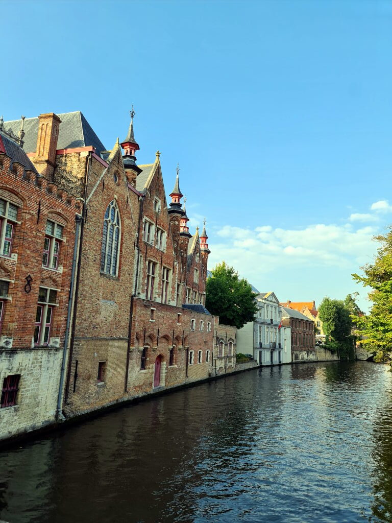 Kanal in Brügge mit historischen Backsteingebäuden und kleinen Türmchen direkt am Wasser unter blauem Himmel