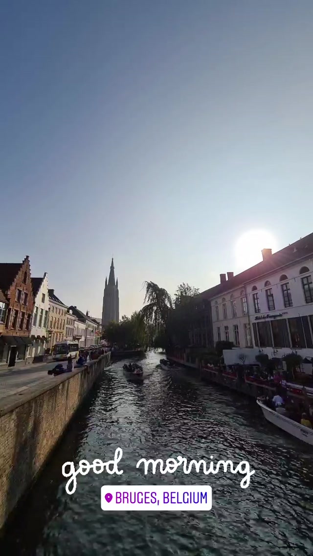 Kanal in Brügge im frühen Morgenlicht mit der Silhouette der Liebfrauenkirche im Gegenlicht der aufgehenden Sonne, ein Ausflugsboot auf dem Wasser