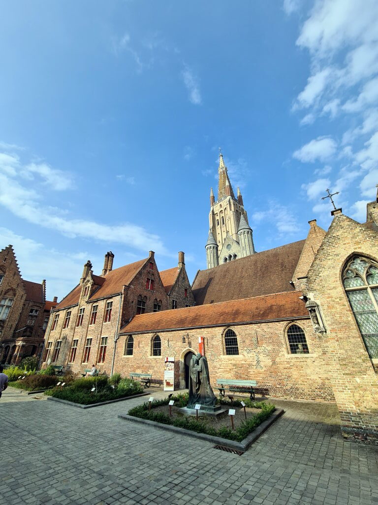 Der Innenhof des Sint-Janshospitaal in Brügge mit einer Bronzestatue, Backsteingebäuden und dem Turm der Liebfrauenkirche im Hintergrund