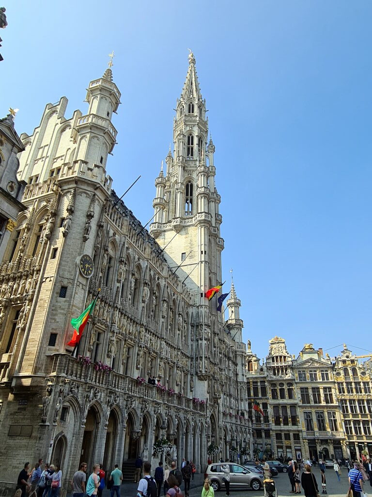Das gotische Rathaus am Grand Place in Brüssel mit seinem hohen Turm unter blauem Himmel, belgische und EU-Flaggen wehen an der Fassade