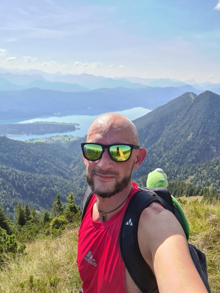 Selfie auf dem Gipfel mit Walchensee im Hintergrund, roter Wanderer mit Kermit, September 2021