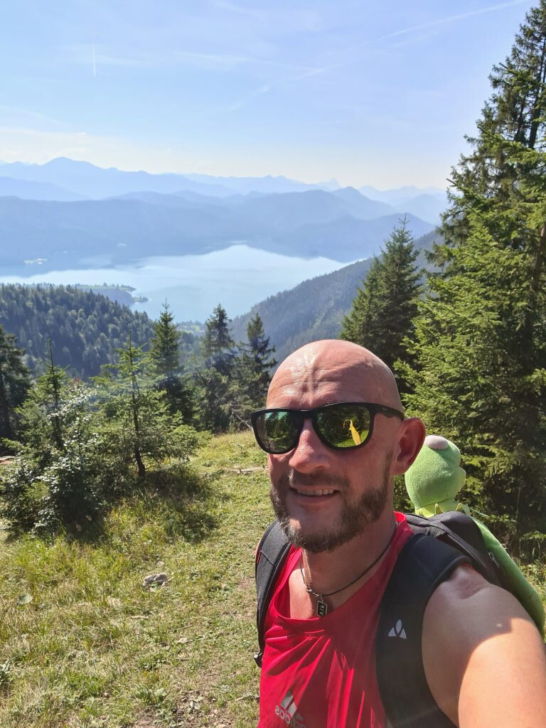 Selfie mit Walchensee im Hintergrund, Wanderer mit rotem Shirt und Kermit im Rucksack, September 2021